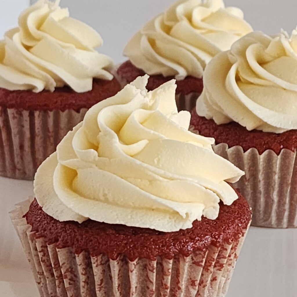 photo of multiple vegan red velvet cupcakes showing the detail of the cake and intricate piping